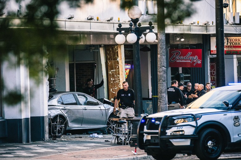 A silver car rests heavily damaged after crashing into the storefront of a business named 'Bradley's' in Ybor City. Police and State Troopers are gathered at the scene, with a patrol car visible in the foreground.