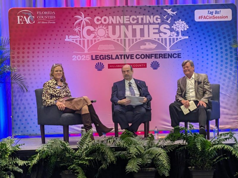 Cragin Mosteller, Steven Geller, and Lee Constantine seated on a stage at the Florida Association of Counties 2025 Legislative Conference in Tampa. The backdrop reads "CONNECTING COUNTIES" and "2025 LEGISLATIVE CONFERENCE."